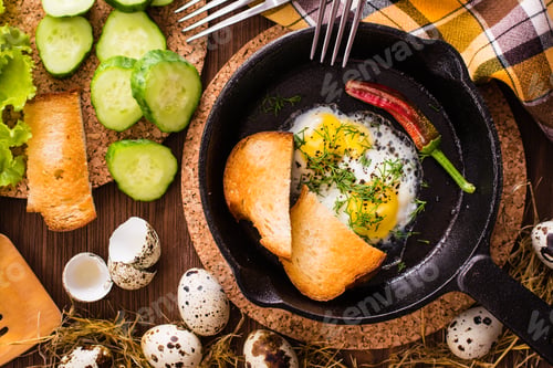 Preview: Close up of fried quail eggs in a iron pan, cucumber, pepper and bread