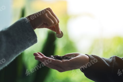 Preview: Closeup image of a hand putting coins into another people's hands
