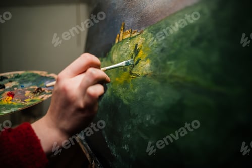 Preview: woman artist paints a picture with oil paints on canvas and palette in hand