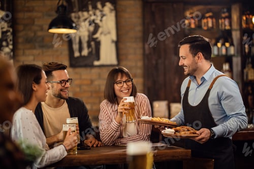 Preview: Group of happy friends drinking beer while waiter is serving them food in a pub.