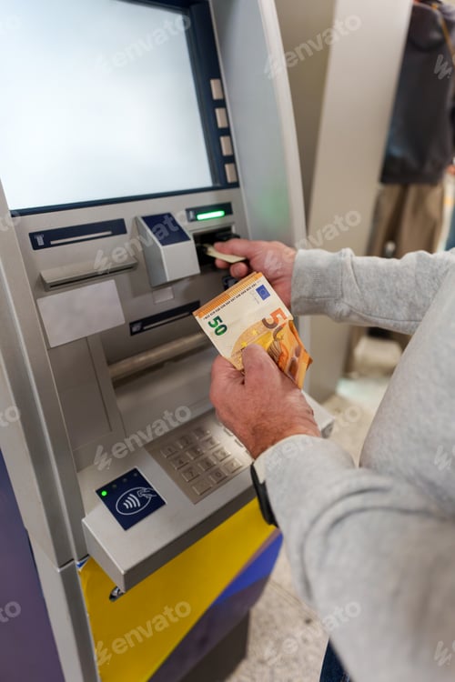 Preview: Senior man withdrawing cash from an ATM and holding fifty euro banknotes, managing personal finance