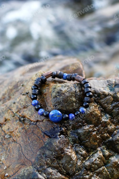 Preview: Bangle made from black agate, blue lazurite and wooden elements on a wet stone near to sea.