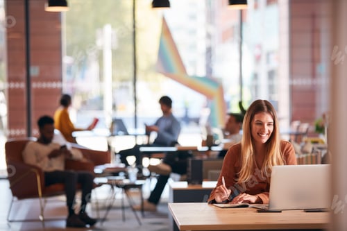 Preview: Young Businesswoman Sitting At Desk Writing In Notebook In Modern Open Plan Office