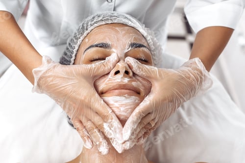 Preview: Cosmetologist applying cream on female face in cosmetology salon.