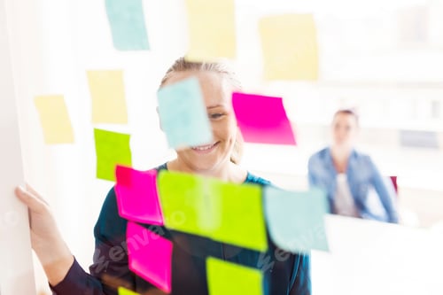 Preview: A woman smiling at colorful sticky notes on a glass wall in an office setting