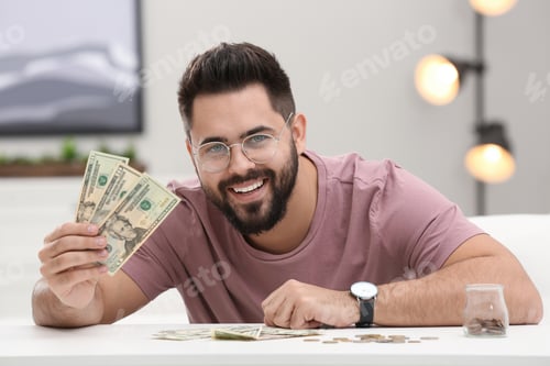 Preview: Happy young man with money at white table indoors