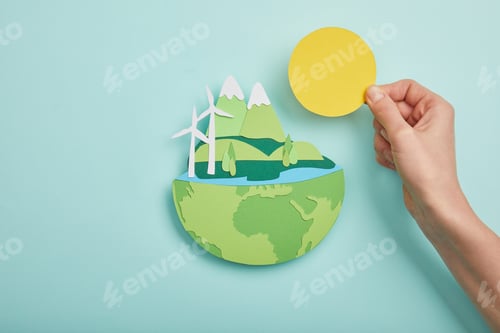Preview: top view of woman holding paper cut sun and planet with renewable energy sources on turquoise