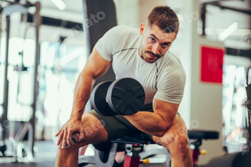 Preview: A young strong man is doing exercises for his biceps with heavy weights in a gym.