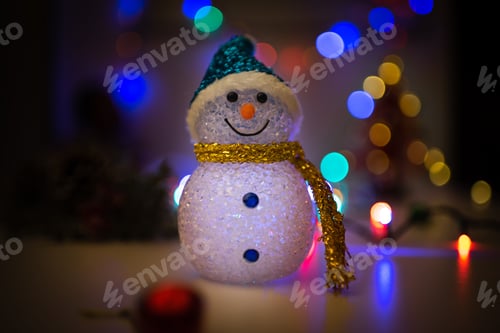 Preview: Festive snowman toy on a tabletop with colorful Christmas lights in the background.