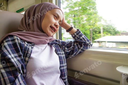 Preview: happy asian muslim woman sitting and looking outside through big window