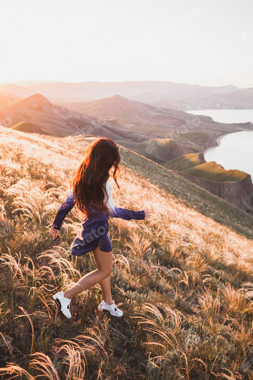 Preview: Happy young woman running on feather grass field in sunset light. Nature lifestyle and amazing view