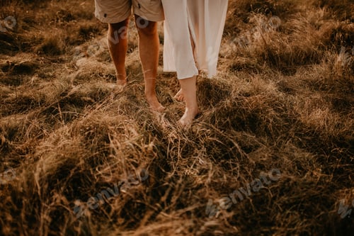 Preview: tanned man and light skin legs woman barefoot close-up walking on dry green thin grass.