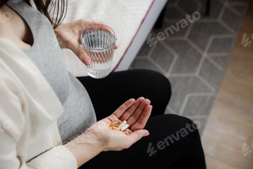 Preview: Pregnant woman holding glass of water, heap of pills in hand. Pregnancy health