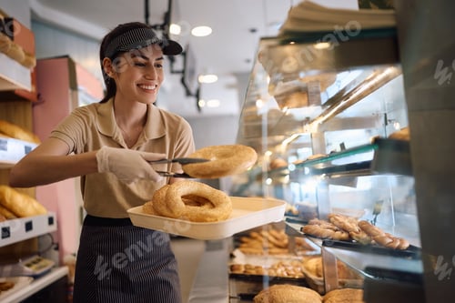Preview: Happy female bakery worker arranging fresh pasty.