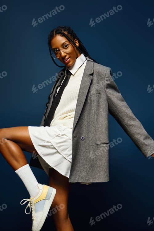 Preview: A confident young woman poses in a chic oversized blazer against a deep blue backdrop.