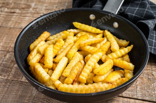 Preview: Deep fried Crinkle French fries potatoes sticks in a pan. Wooden background. Top view