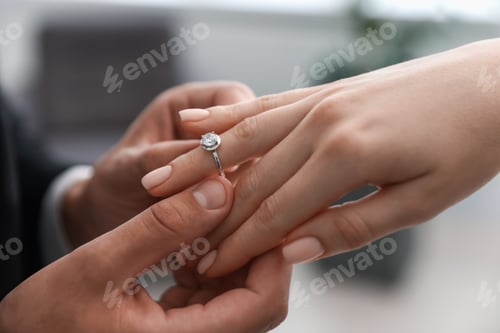 Preview: Making proposal. Man putting engagement ring on his girlfriend's finger indoors, closeup