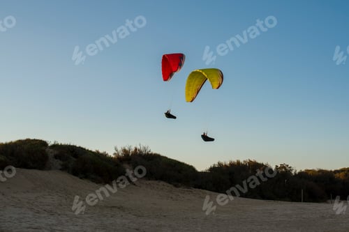 Preview: Two paragliders soaring above the scenic sand dunes at sunset