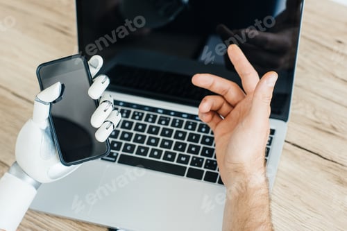 Preview: cropped shot of human and robot hands using smartphone and laptop with blank screens