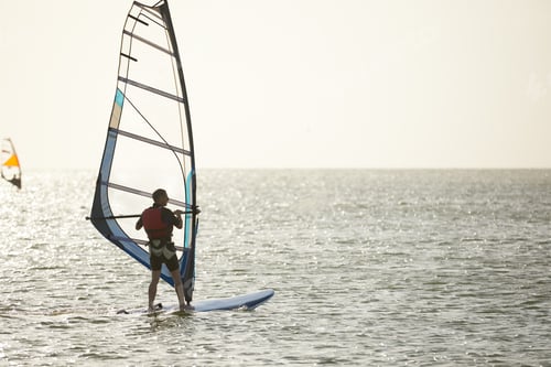 Preview: Windsurfer against the backdrop of the setting sun, on calm water, goes calmly along the sea, active
