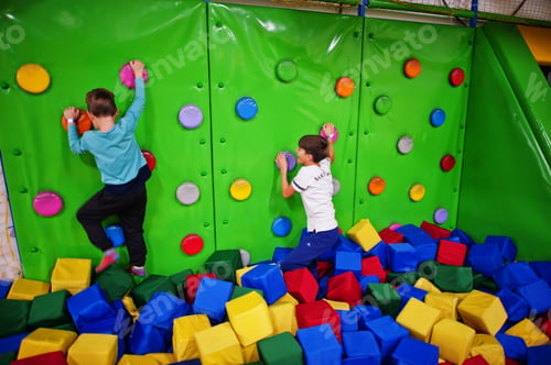 Preview: Two brothers kids climbing on a green wall in attraction playground.