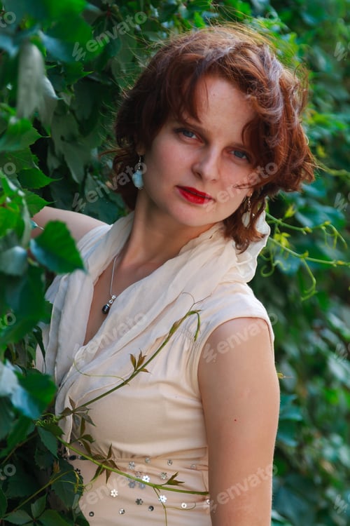 Preview: Beautiful girl in a light beige dress in green leaves
