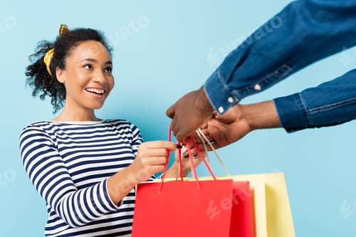 Preview: cheerful african american wife taking shopping bags from husband on blue