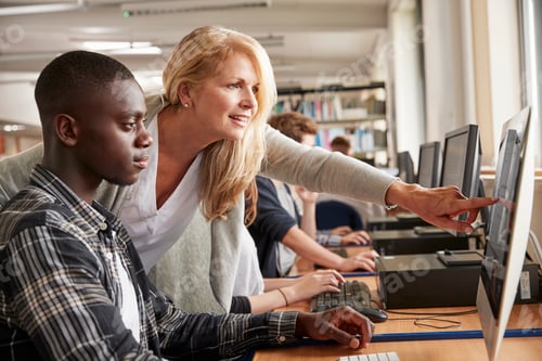 Preview: Teacher With Male Student Working On Computer In College Library