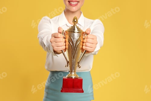 Preview: Young businesswoman with gold trophy cup on yellow background, closeup