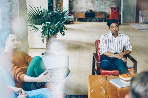 Preview: Serious black woman listening comfortably sitting in chair with crossed leg