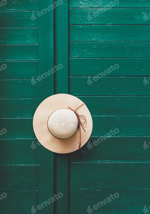 Preview: Minimalist image of summer hat hanging on door handle on green wooden door.