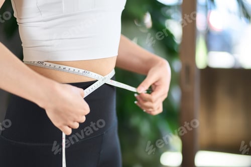 Preview: Asian woman measuring her waist size with a tape measure