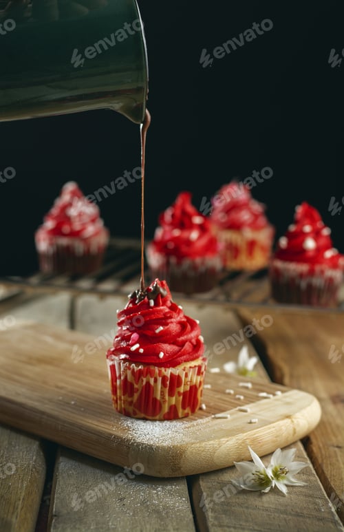 Preview: Vertical shot of a person pouring chocolate cream on a cupcake with red cream