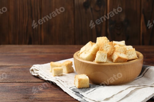Preview: Delicious crispy croutons in bowl on wooden table. Space for text
