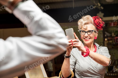Preview: Quirky vintage woman photographing boyfriend in antiques emporium