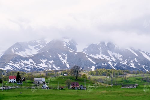 Preview: Small village in a green valley at the foot of snow-capped mountains