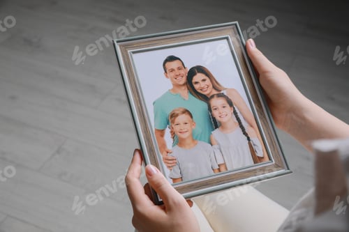Preview: Woman holding framed family photo indoors, closeup