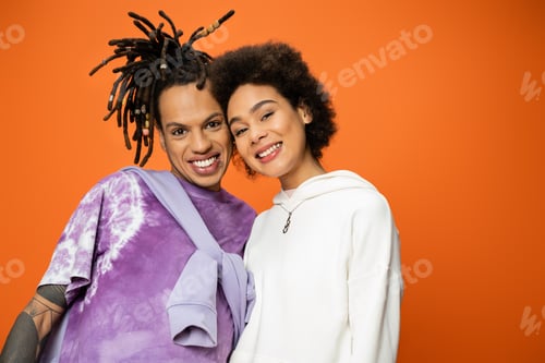 Preview: happy african american woman looking at camera near stylish friend with dreadlocks isolated on