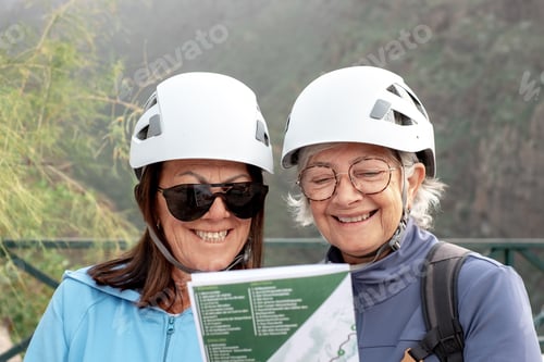 Preview: Smiling senior women hikers with helmets standing on the top of mountain looking at