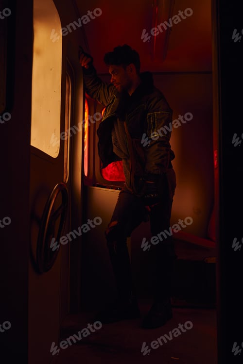 Preview: man with gun looking through window of abandoned carriage in post-disaster subway with red light