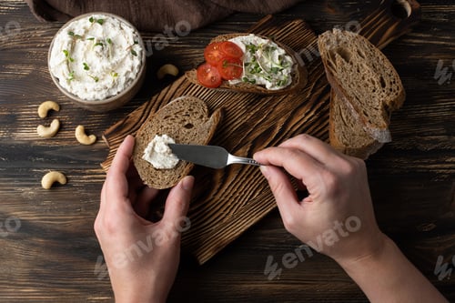 Preview: Female hands spreading vegan cashew cream cheese on a slice of bread.