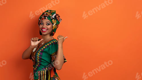 Preview: Stunning black woman in african costume pointing at copy space
