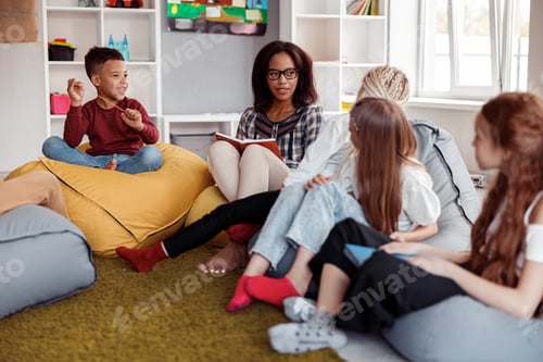 Preview: Female teacher sitting on a pouf and reading for schoolchildren