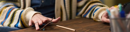 Preview: Hands of Young Man Playing with Miniature Skateboard at Desk