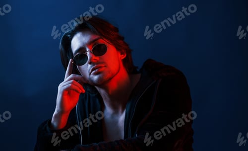 Preview: Beautiful man in glasses and black clothes is in the studio with blue neon lighting