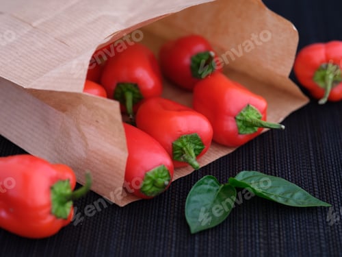 Preview: Some red bell peppers lying in a paper bag with some leaves near it