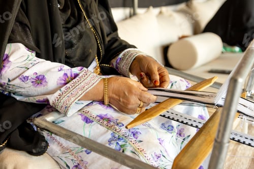 Preview: Senior Emirati woman using traditional weaving machine, hands in frame