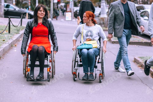 Preview: Two girls on wheelchairs in the city near the walking men of the townspeople.