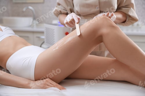 Preview: Cosmetologist applying gel on client's leg before depilation procedure in beauty salon, closeup