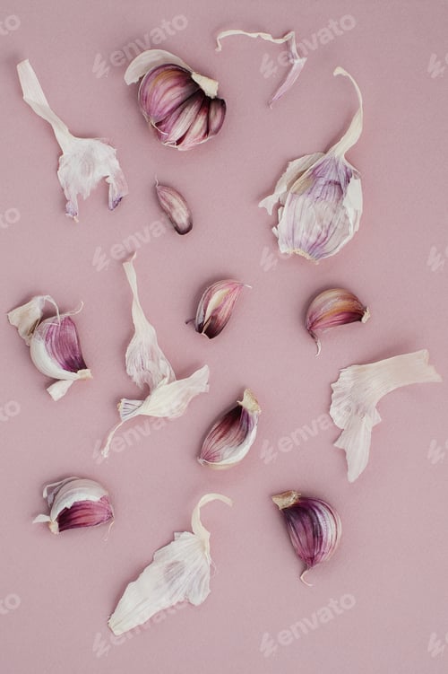 Preview: The cloves of garlic are scattered on a light pink background.